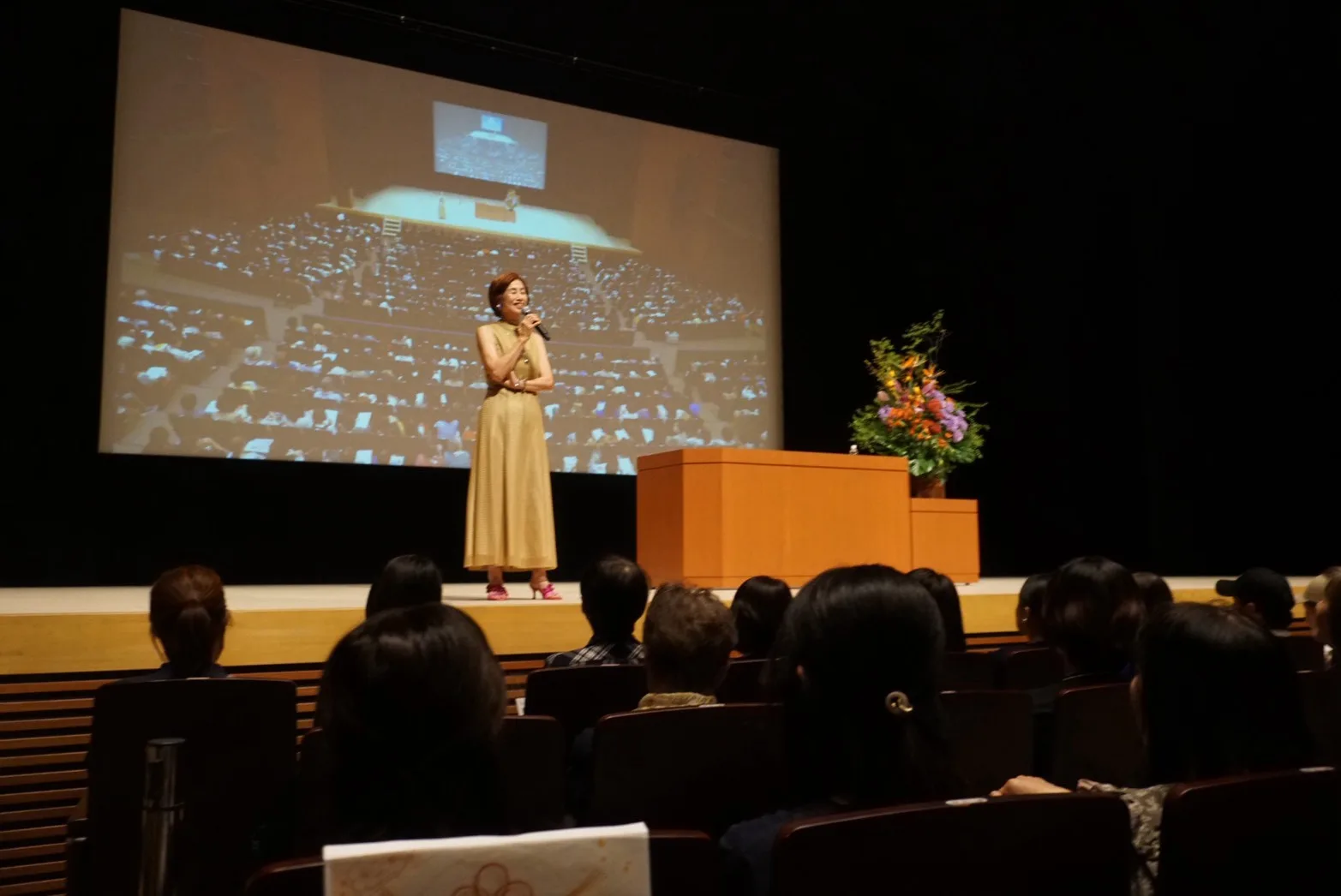 客席から見た舞台。スクリーンの前で話すやましたひでこさん